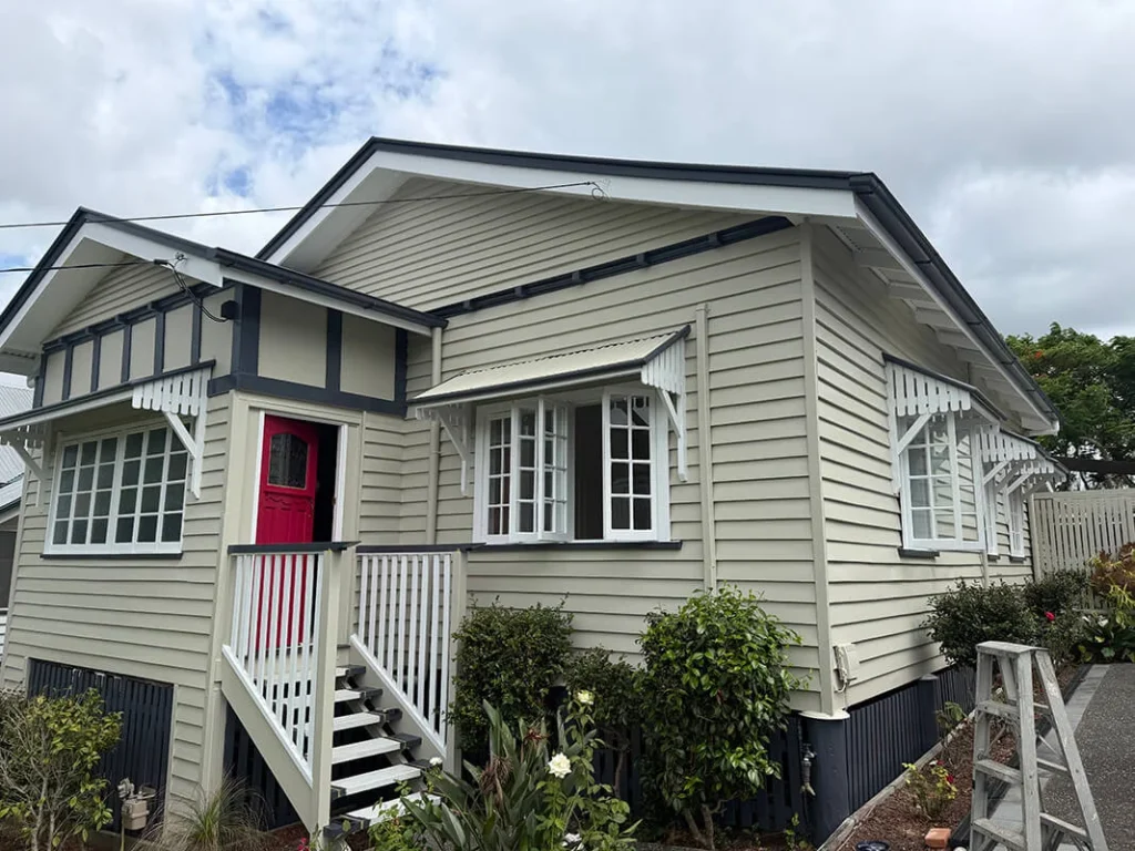 Exterior house painting completed on a Queenslander in beige and charcoal with a red front door